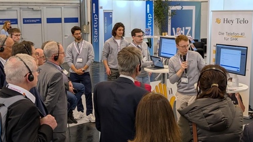 Teilnehmer eines Messerundgangs verfolgen eine Präsentation am Stand von Hey Telo.